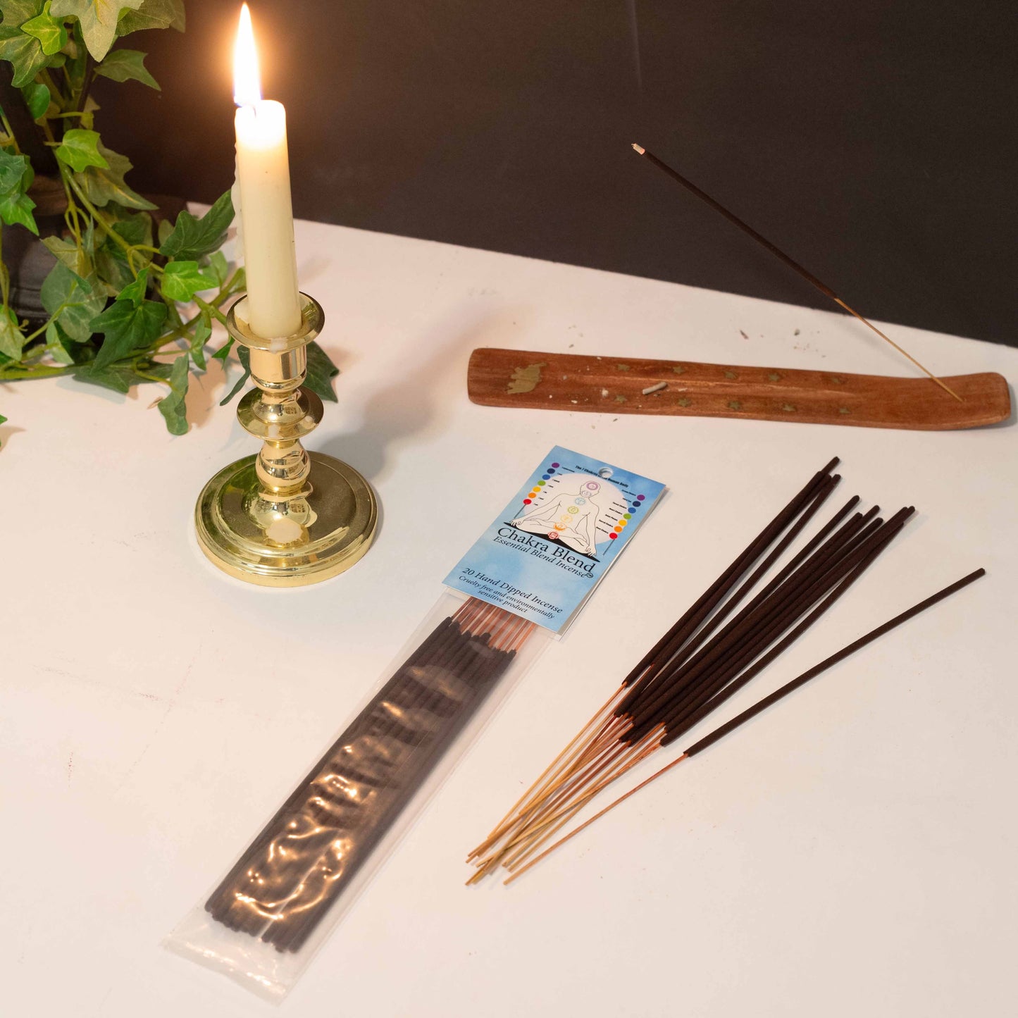Chakra Blend stick incense with burning incense in holder, candle, and greenery on a white surface